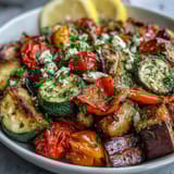 Roasted Mediterranean Greek vegetables plated as a main dish, topped with feta and parsley alongside warm pita bread.