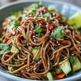 Chilled soba noodles tossed with colorful vegetables and a creamy sesame ginger dressing, garnished with fresh cilantro and sesame seeds.  
