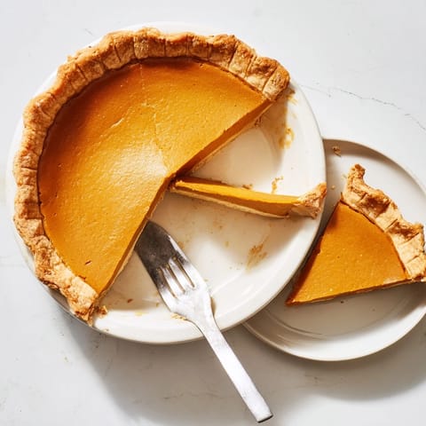 A slice of creamy pumpkin pie on a white plate, topped with a dollop of whipped cream and a sprinkle of cinnamon.