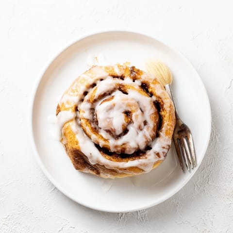 Golden, fluffy cinnamon rolls topped with creamy glaze on a rustic kitchen counter.  