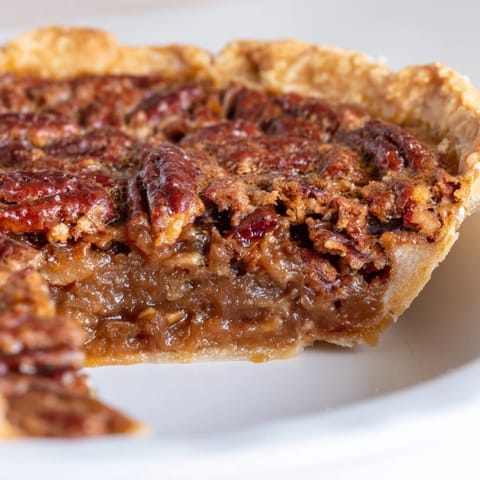 A slice of Southern pecan pie being lifted from the whole dessert, revealing the rich, gooey brown sugar and corn syrup custard packed with crunchy pecan halves.  