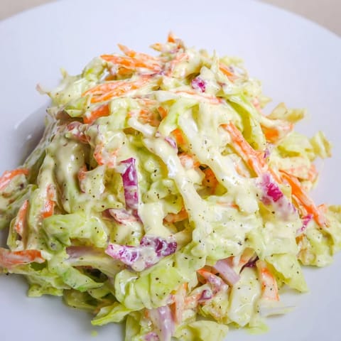 Classic American Coleslaw chilled and ready to serve, with tangy mayonnaise dressing and crunchy red onion slices on a plate.