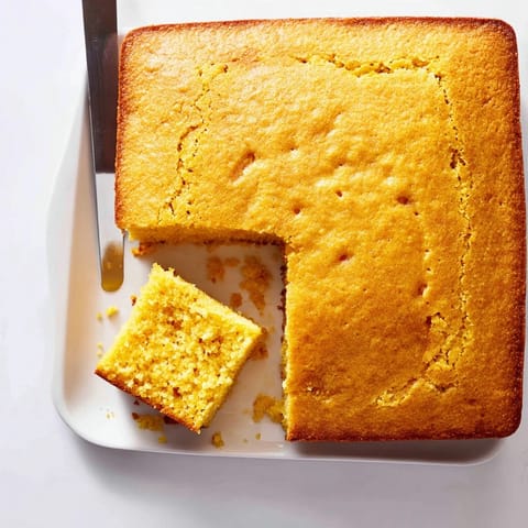 Freshly sliced square of cornbread with a crispy crust, drizzled with honey butter on a rustic wooden board.