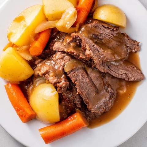 Slow-cooked beef pot roast with tender potatoes, carrots, and onions in a rich, savory gravy on a rustic platter.  