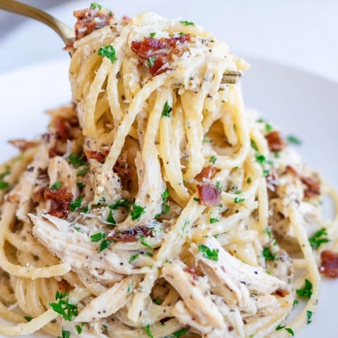 Close-up of Chicken Carbonara pasta twirled on a fork, with crispy bacon bits and tender shredded chicken coated in a creamy, golden Parmesan-egg sauce.
