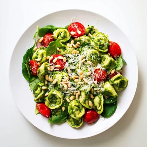 A close-up of chilled Pesto Tortellini Salad garnished with toasted pine nuts and grated Parmesan, offering a refreshing and easy vegetarian meal for warm summer days.