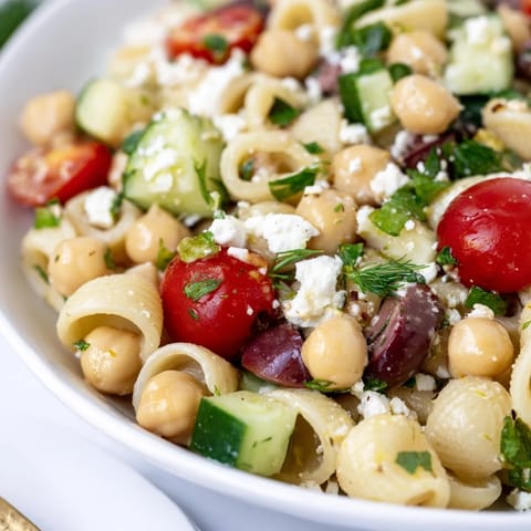 Fresh lemon herb chickpea pasta salad with diced cucumbers, cherry tomatoes, and chopped herbs in a glass bowl.