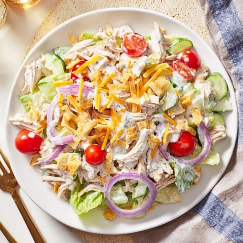 Spicy jalapeño ranch chicken salad served in a white bowl, garnished with cheddar cheese and crispy tortilla strips.