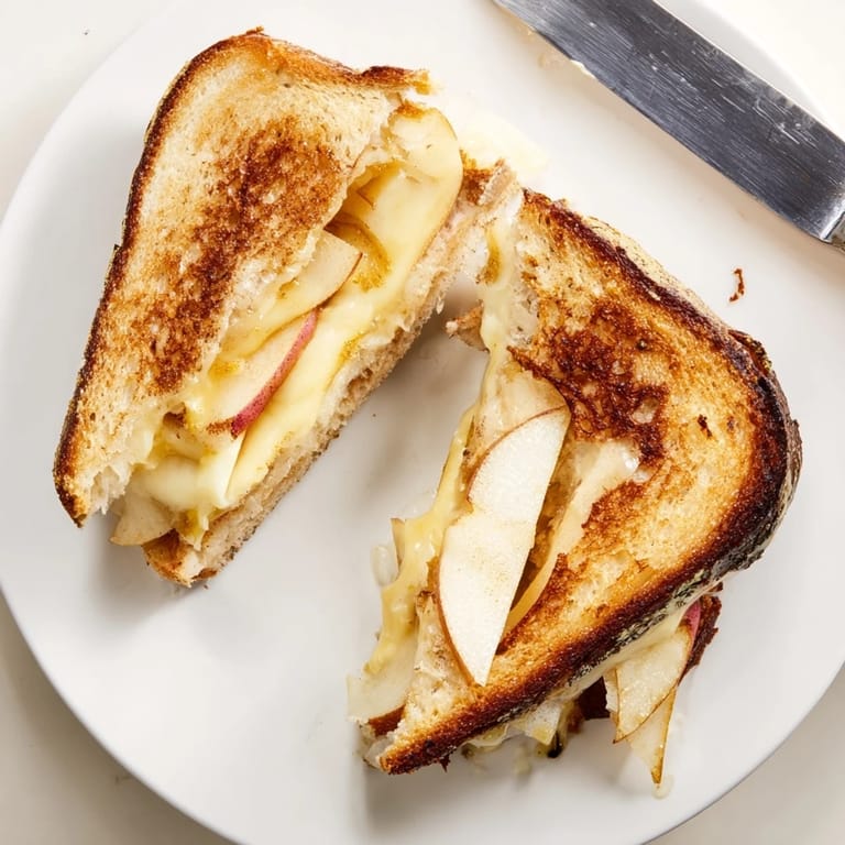 Close-up of a warm Smoked Gouda & Apple Grilled Cheese, highlighting the gooey smoked cheese and thin, fresh apple layers between toasted bread.  