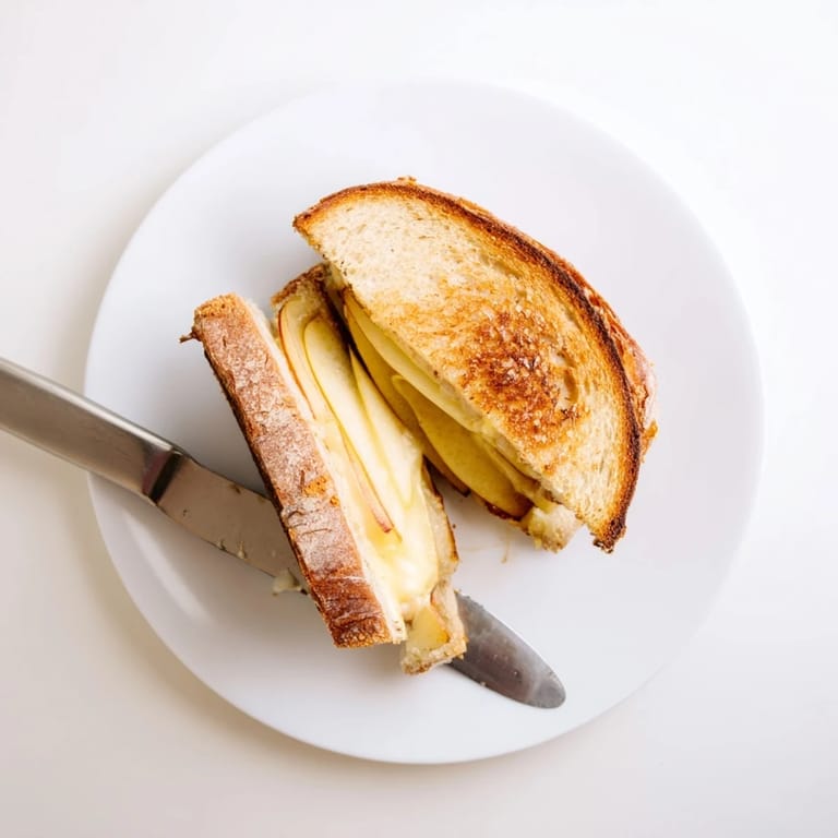 A gourmet Smoked Gouda & Apple Grilled Cheese cut in half, revealing steamy melted cheese and crisp apple slices, served beside a cozy bowl of tomato soup.