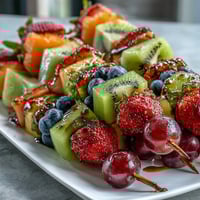 Colorful rainbow fruit skewers featuring strawberries, pineapple, kiwi, blueberries, and grapes served with a creamy honey-yogurt dip for a refreshing summer snack.